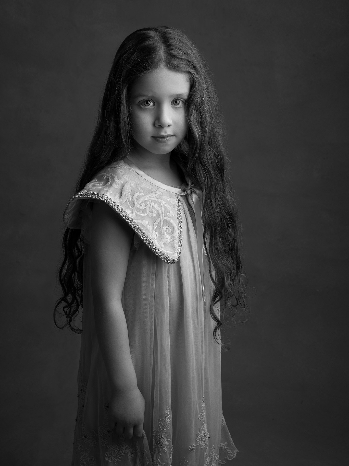 Svartvit bild på flicka med långt och lockigt hår, hon tittar fint in i kameran.