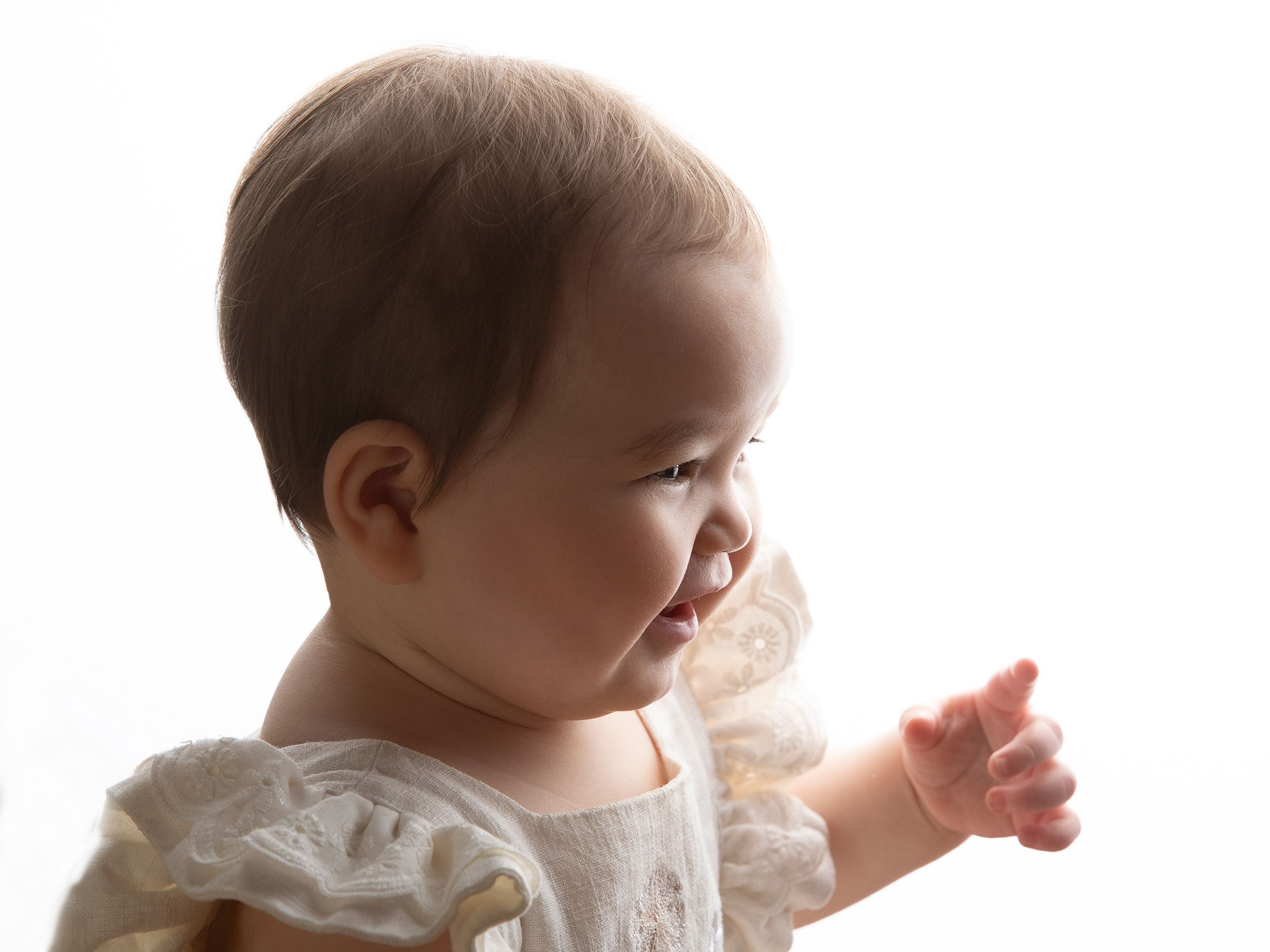 Busig baby ler, sittandes i profil.