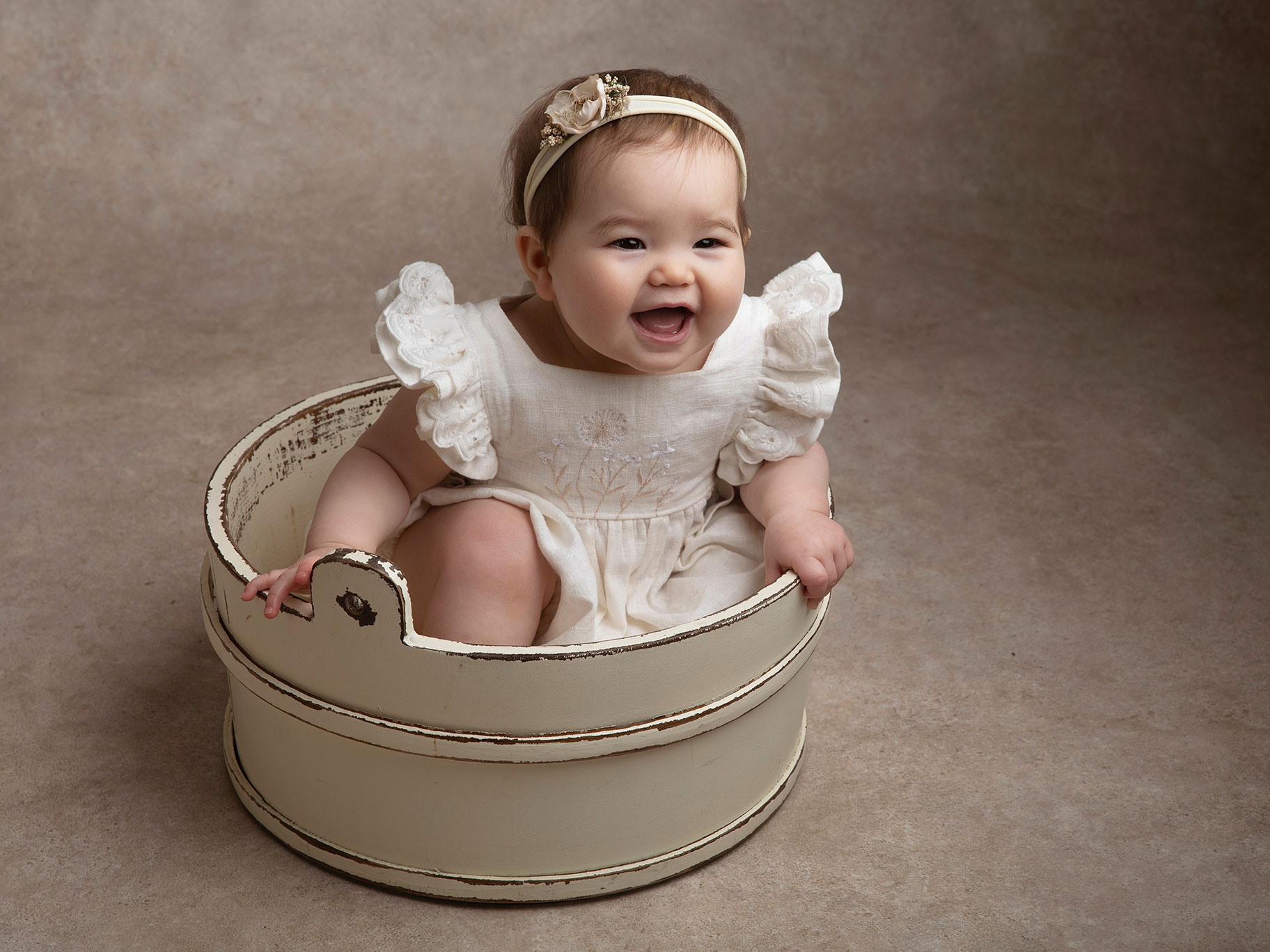 Busig baby skrattar, sittandes i en balja under en fotografering i Malmö.