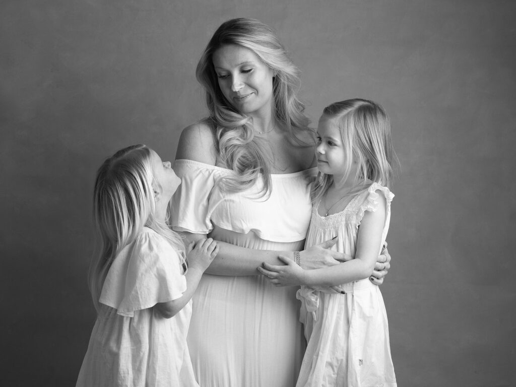 Mamma med två små flickor, de tittar på varandra och ler.