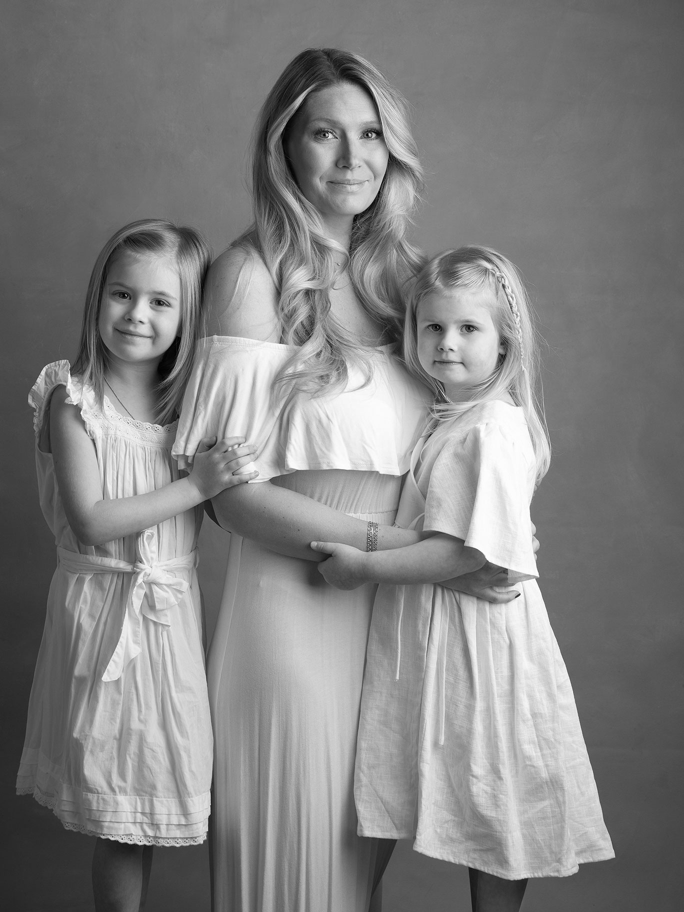 Mamma med två flickor, de tittar mot kameran och ler.