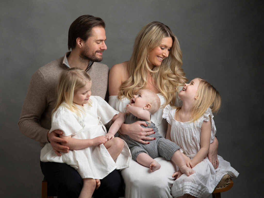 Underbar bild på en familj med tre små barn, alla tittar på varandra och ler.