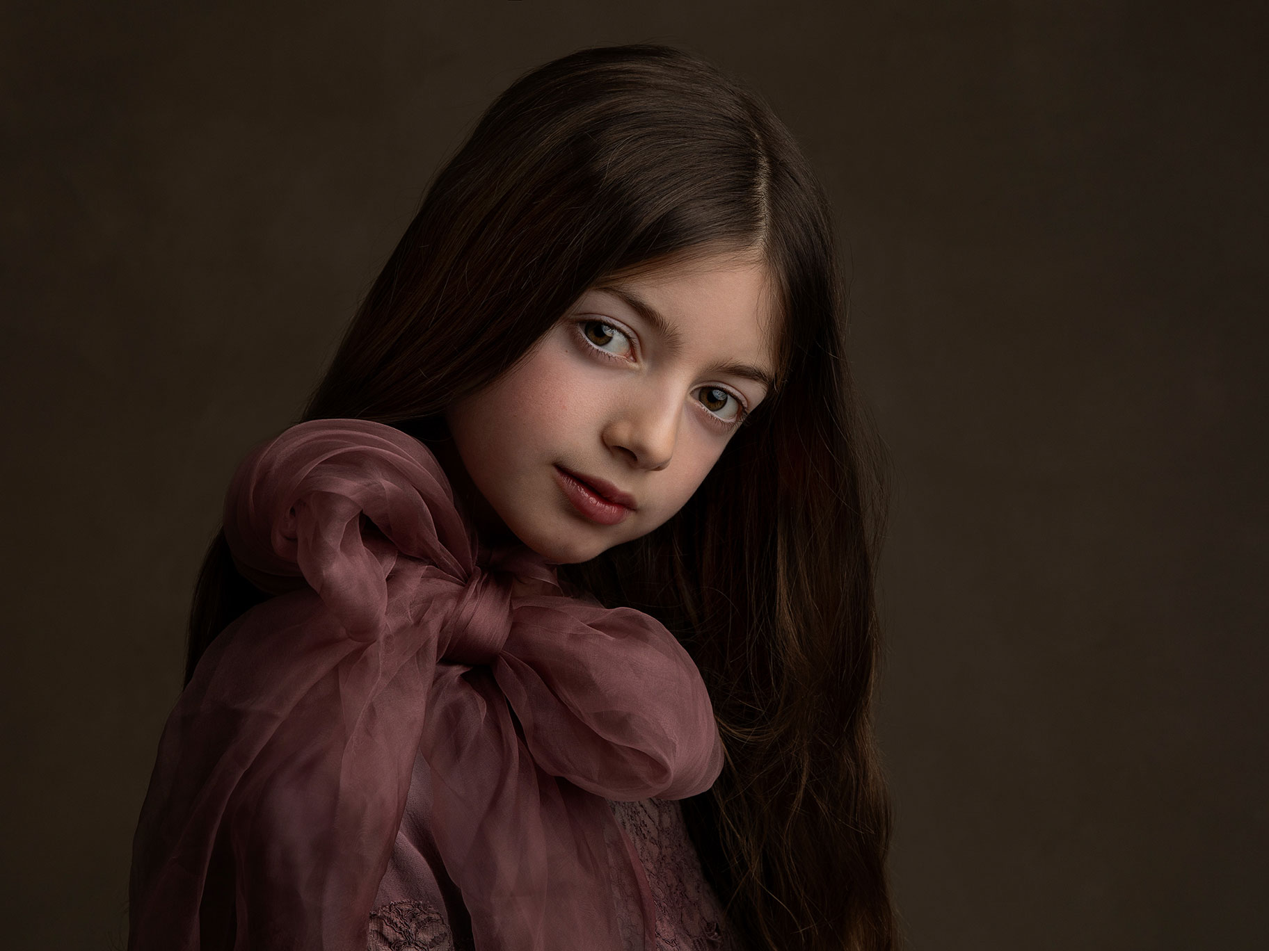 Vacker och konstnärlig bild av en flicka med brunt långt hår med stor lila rosett vid halsen.