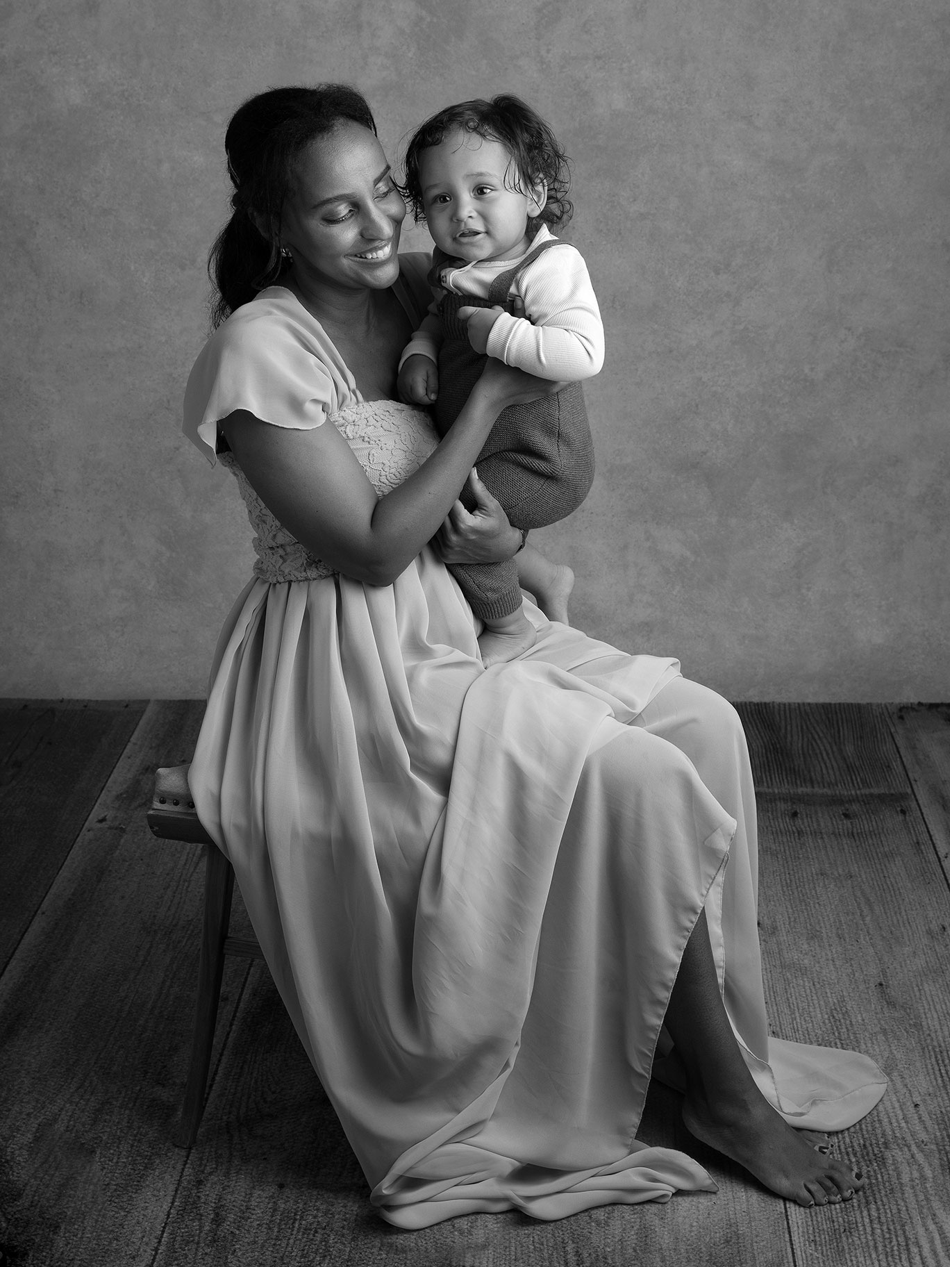Mamma har sin son i knäet framför fotografen i en studio i Skåne.